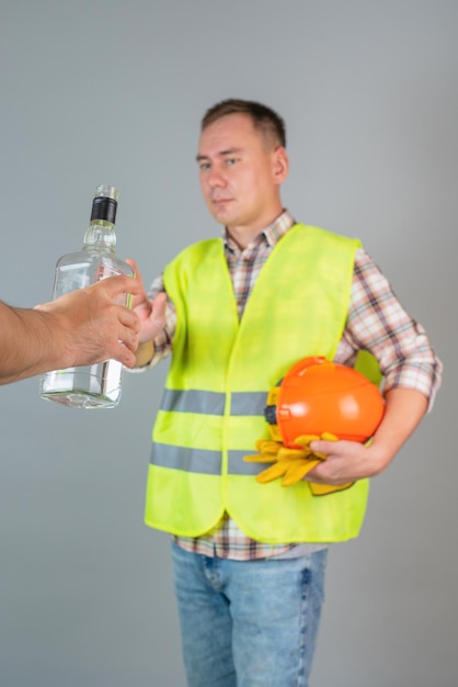 作業服を着た男性の建設労働者は、提供された強いアルコールのボトルを拒否します