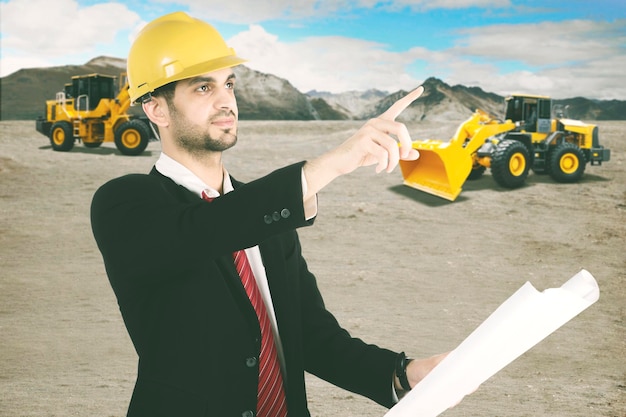 Male contractor holding blueprint pointing on construction site