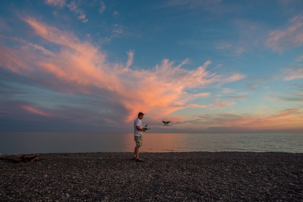 The male controls a quadrocopter on the sunset background