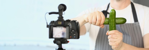 Male cook blog holding two cucumbers in front of camera