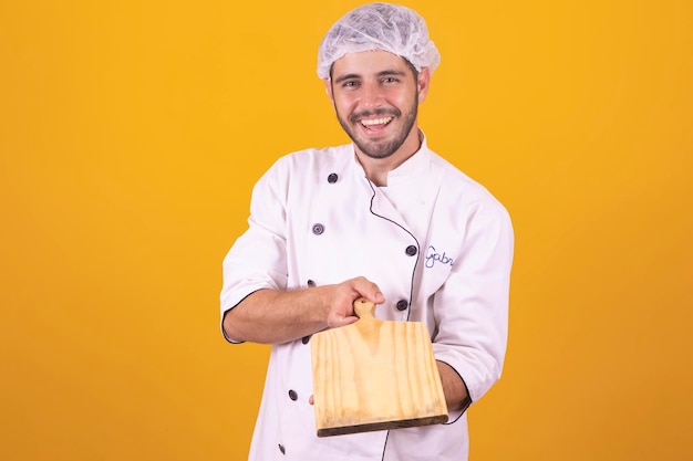 Male cook chef holding a cutting board isolated over yellow background