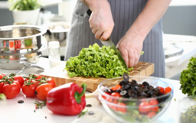 Foto il cuoco fa l'insalata di verdure e taglia le foglie di lattuga verde