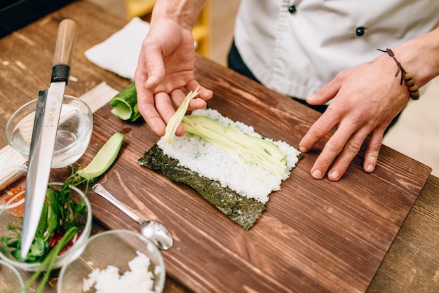 Male cook making sushi rolls on wooden table, seafood. Traditional japanese cuisine, preparation process