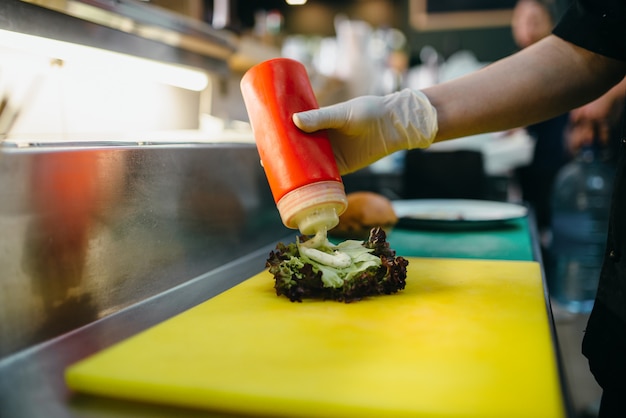 Male cook prepares fresh salad for burger