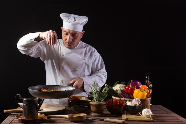 男性は白い制服を着て料理し、帽子は野菜と一緒にフードプレートにハーブを置きます