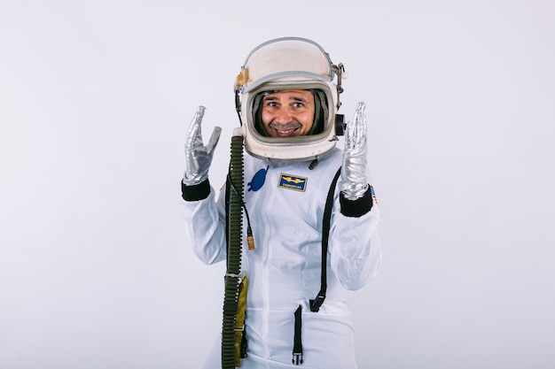 Male cosmonaut in space suit and helmet, raising his hands with gesture of fun, on white background.