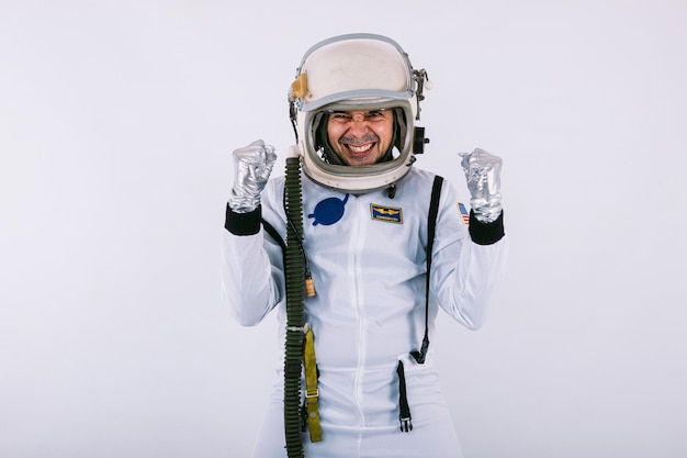 Male cosmonaut in spacesuit and helmet, clasping hands in a sign of joy and strength, on white background.