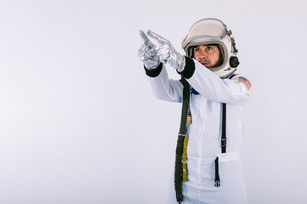 Male cosmonaut in spacesuit and helmet, pointing finger to the sky, on white background.