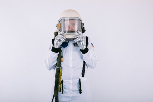 Male cosmonaut in spacesuit and helmet, with surprised face holding the helmet with his hands, on white background.