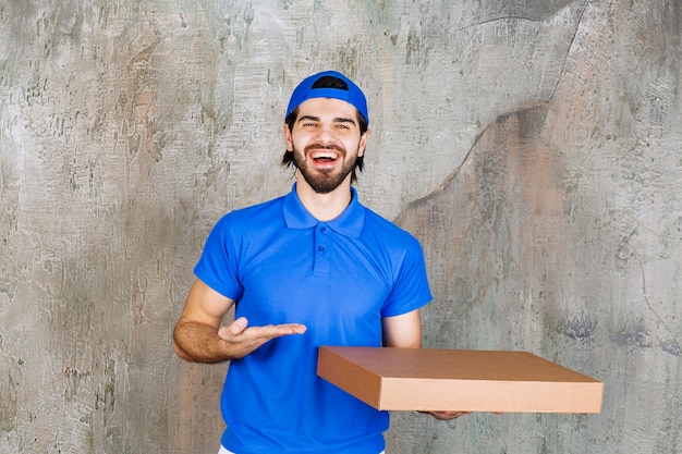 Male courier in blue uniform carrying a cardboard takeaway box .