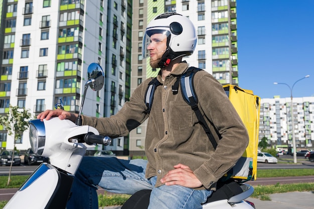 A male courier delivers food in a yellow box on a scooter outside