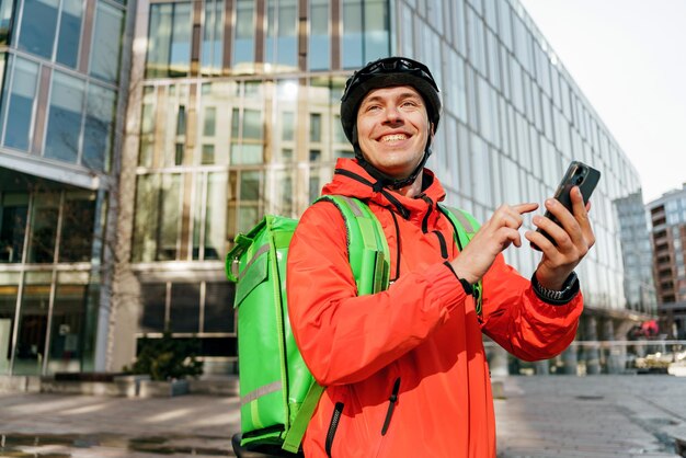 A male courier in a helmet and with a thermo bag uses the Navigator app to deliver an order