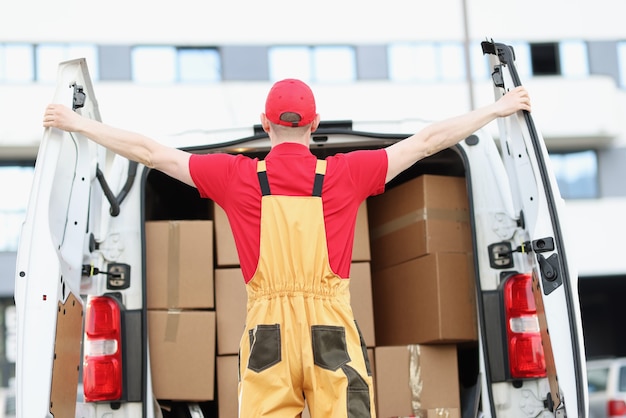 Male courier opening minivan car with many cardboard boxes