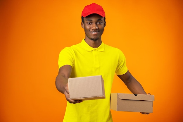 Male courier wearing uniform holding box in orange studio