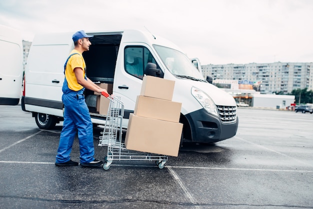 Corriere maschio con carrello pacchi contro camion con scatole di cartone. attività di distribuzione. consegna del carico. contenitori vuoti e trasparenti. logistica e servizio postale