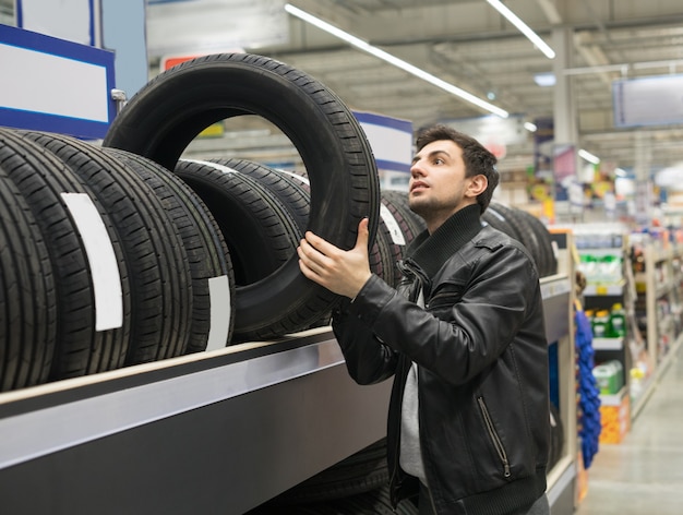 Male customer choosing new tires in the supermarket. He is taking tire from shelf