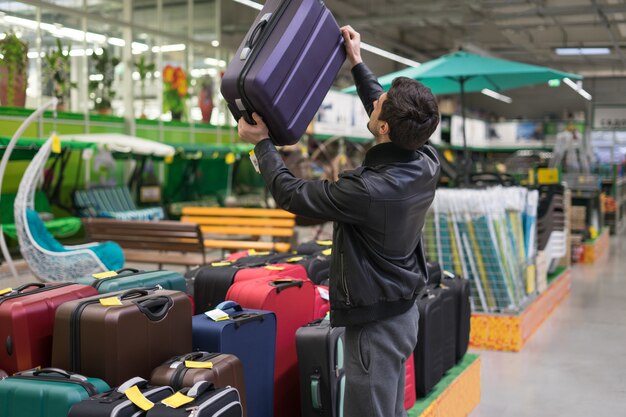 Cliente maschio che sceglie valigia da viaggio al supermercato. prese la borsa.