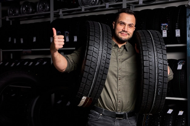 Male customer is satisfied with purchase of tyre in automobile repair garage, stand holding rubber for car in hands,in auto store shop