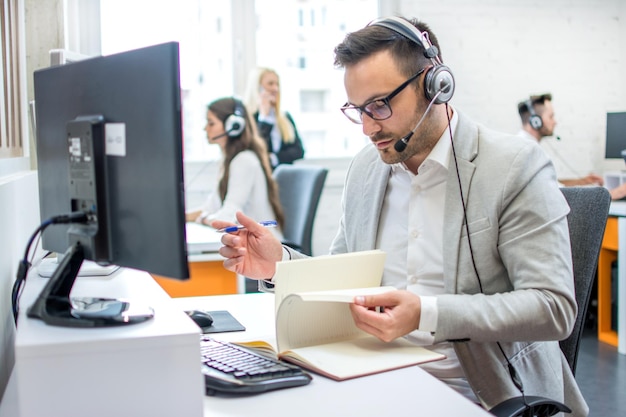 Male customer support operator taking notes while talking with client in call center