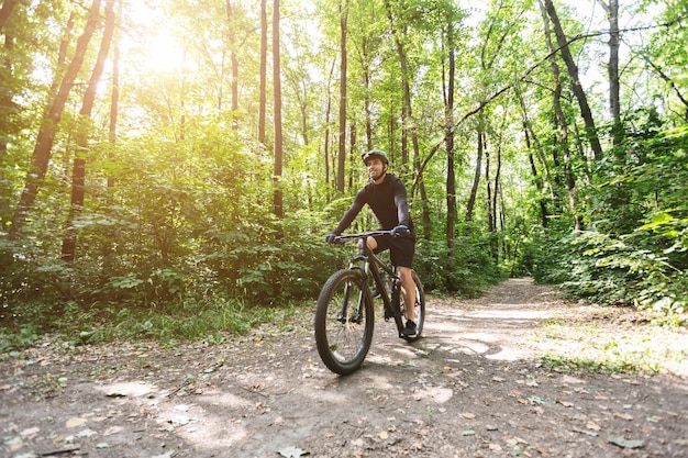 Male cyclist riding on forest trails in sun flare