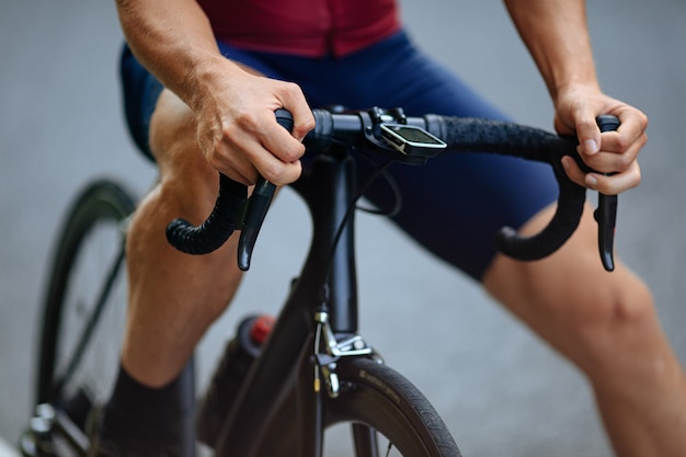 Male cyclist on sport clothing posing with black bike.