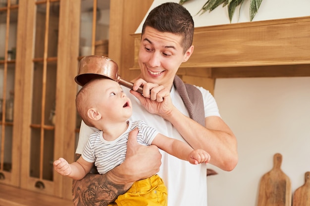 Un papà maschio tiene in braccio un figlio piccolo e cucina a casa in cucina