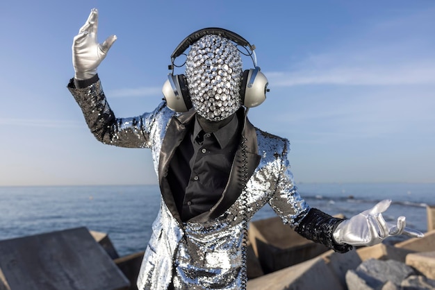 Male dancer in sparkling disco suit and mask by the sea