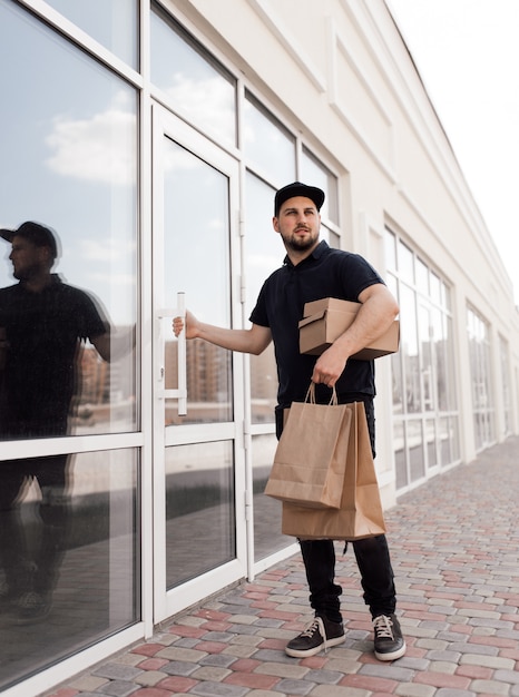 Male delivery man in black uniform with bags