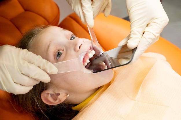 Foto il dentista maschio piegato su un bambino guarda la sua mascella bambino durante la visita dell'ortodontista e il controllo della cavità orale cura e igiene dei denti dei bambinicorrezione del morso dei denti nella clinica dentale