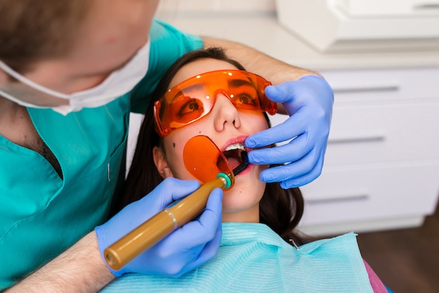 male dentist is filling the tooth with a patient. pretty young girl in a red dental chair. Dental health, tooth enamel