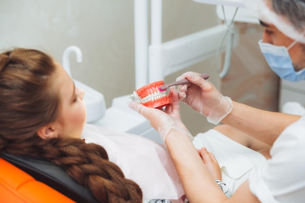 A male dentist in a medical uniform shows a little girl how to properly brush her teeth on a jaw model Dentistry concept