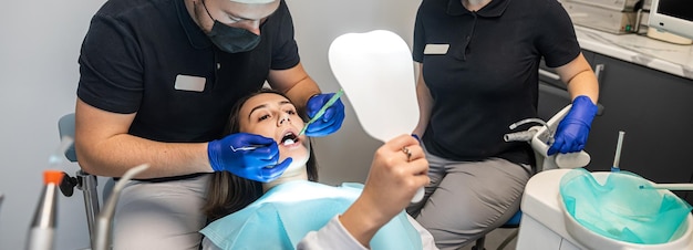 Стоматолог-мужчина оперирует улыбающуюся женщину в стоматологической клинике, а ассистентка помогает ему