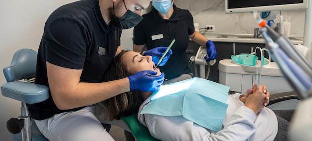 мужской стоматолог оперирует молодую улыбающуюся женщину в стоматологической клинике, и женщина-помощник помогает ему