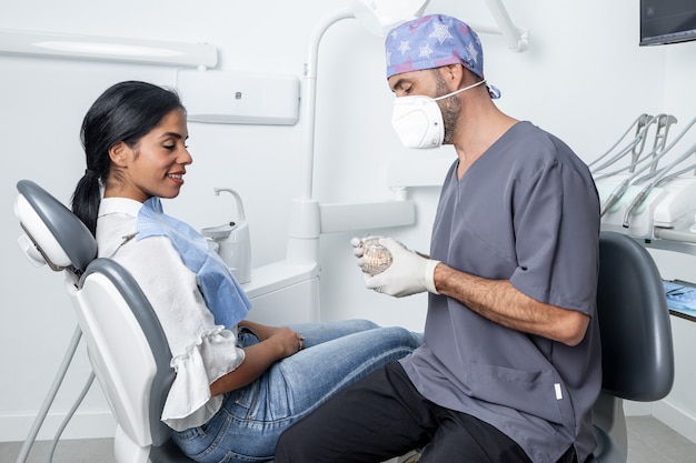 Male dentist showing a dental mould to a female patient sitting in a chair in a dental clinic