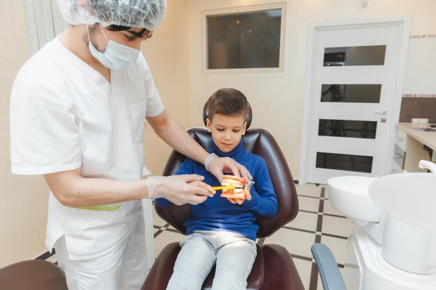 A male dentist shows a boy on a denture how to properly brush his teeth the concept of children's medical examination