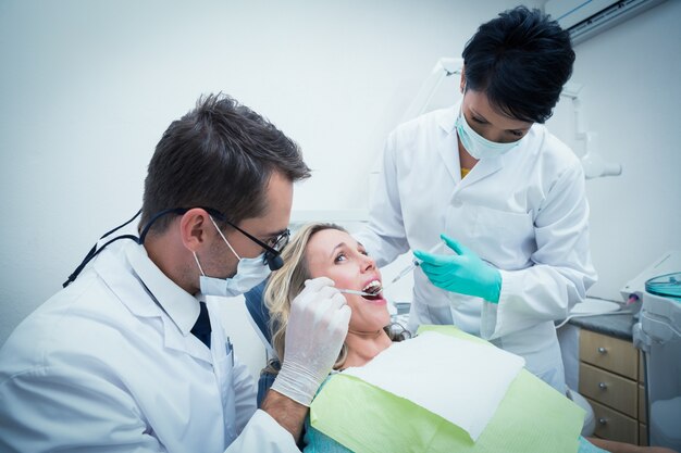 Dentista maschio con l'assistente che esamina i denti dei womans