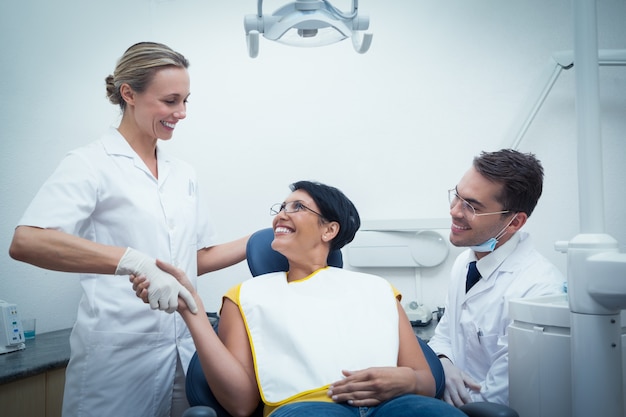 Male dentist with assistant shaking hands with woman