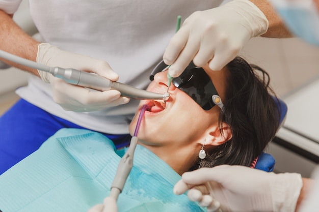 The male dentist with a female assistant helps to treat the teeth of a woman patient in a clinic in the office, close-up