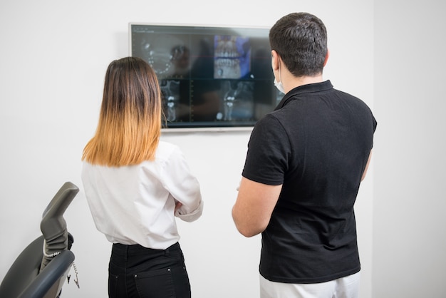 Male dentist with female patient looking at dental x-ray image on computer screen