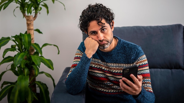 Male depression holding his forehead while having headache on couch home. Adult man using smart phone and thinking, having heavy thoughts, breake up with lover or financial difficulties concept