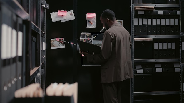 Photo male detective reading witness statements in archive, using surveillance footage to uncover new clues or details. african american man planning criminal investigation to catch suspect. handheld shot.