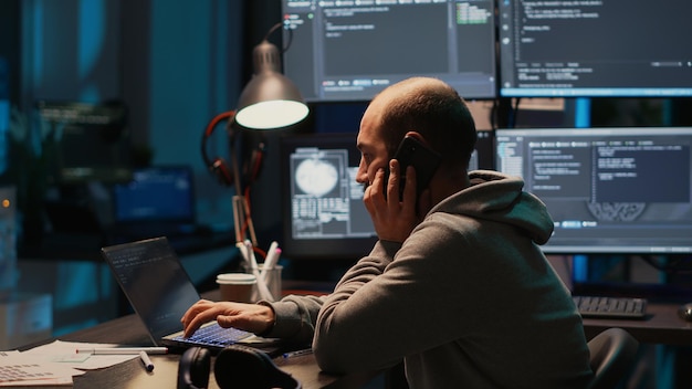 male developer answering phone call in office, talking on smartphone and coding user interface. having remote conversation on mobile phone line, using html script on terminal window.