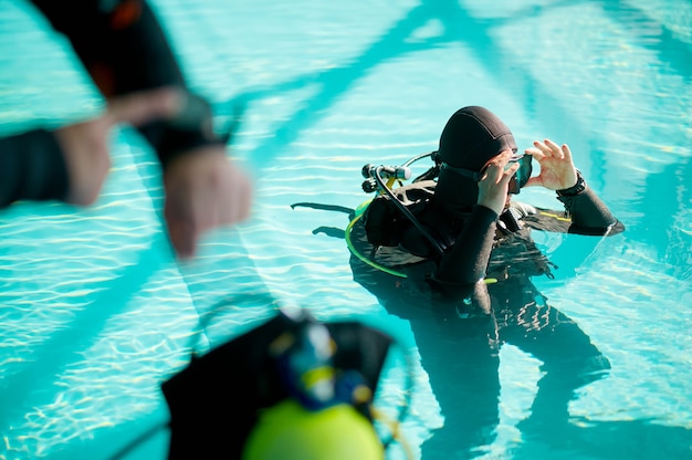 Male diver and divemaster in scuba gear mark the dive time, diving school. Teaching people to swim underwater, indoor swimming pool interior on background