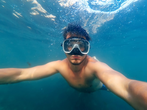 남성 다이버는 마스크를 쓰고 푸른 물 아래 바다에서 수영한다