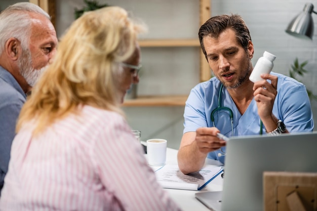 Foto medico maschio che consiglia alle coppie mature degli integratori alimentari e dell'utilizzo di un computer durante l'appuntamento