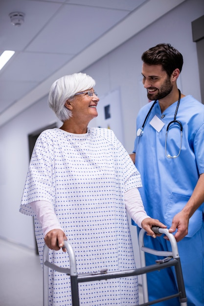 Male doctor assisting senior patient to walk with her walker