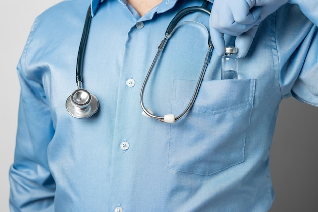 Male, doctor in blue shirt and gloves, holding in the hand vaccine bottle against disease coronavirus or flu, vaccination concept.