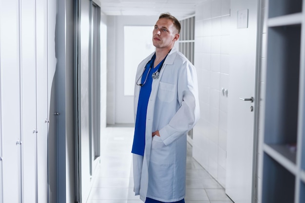 A male doctor in a blue surgical suit and a white coat in the clinic's locker room The beginning of the working day of a professional doctor