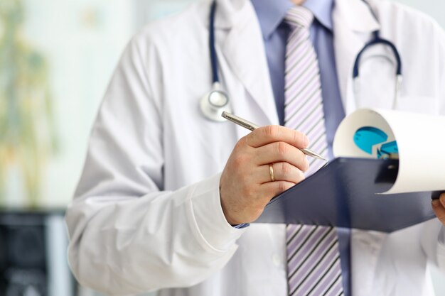 Male doctor checking medical procedure results in document clipped to pad