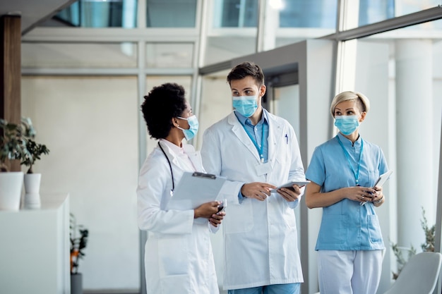 Male doctor communicating with colleagues while standing in a lobby and wearing protective face mask